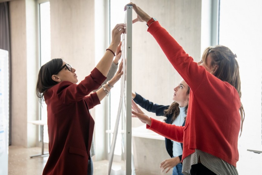 Tre studentesse della Scuola di dottorato in scienze biomediche dell’Università della Svizzera italiana appendono i poster dei loro progetti di ricerca durante il BioMed PhD Day 2022, organizzato al Campus Est di Lugano (foto di Chiara Micci / Garbani)